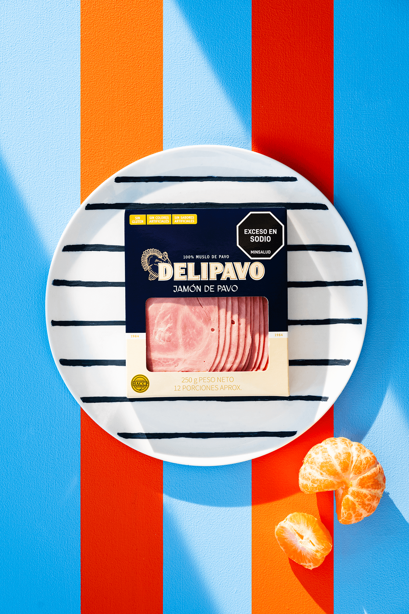 Delipavo Jamón de Pavo presentado en un plato a rayas, acompañado de una mandarina sobre un fondo colorido.