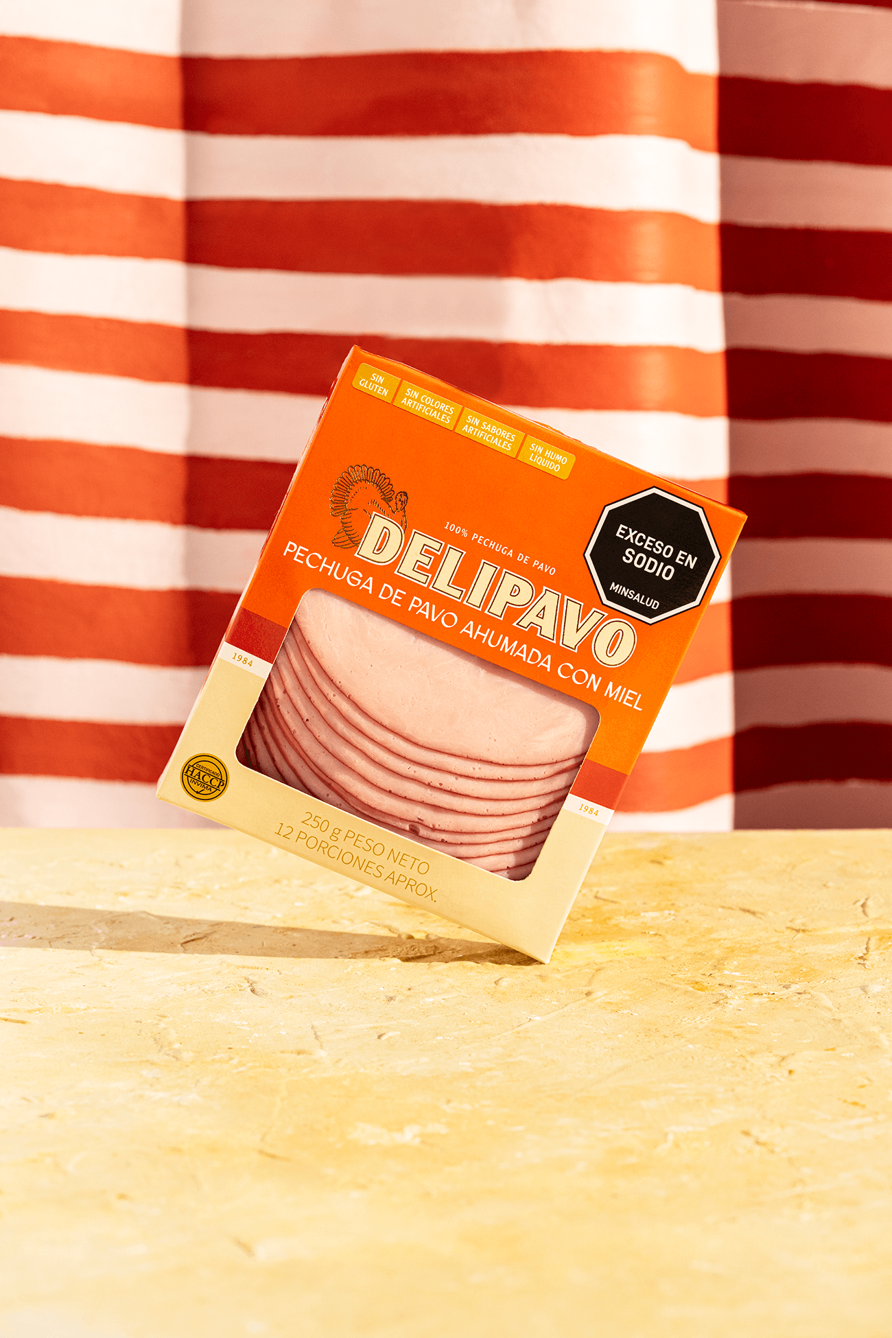 Empaque de Pechuga de Pavo Ahumada con Miel Delipavo sobre mesa con fondo naranja.