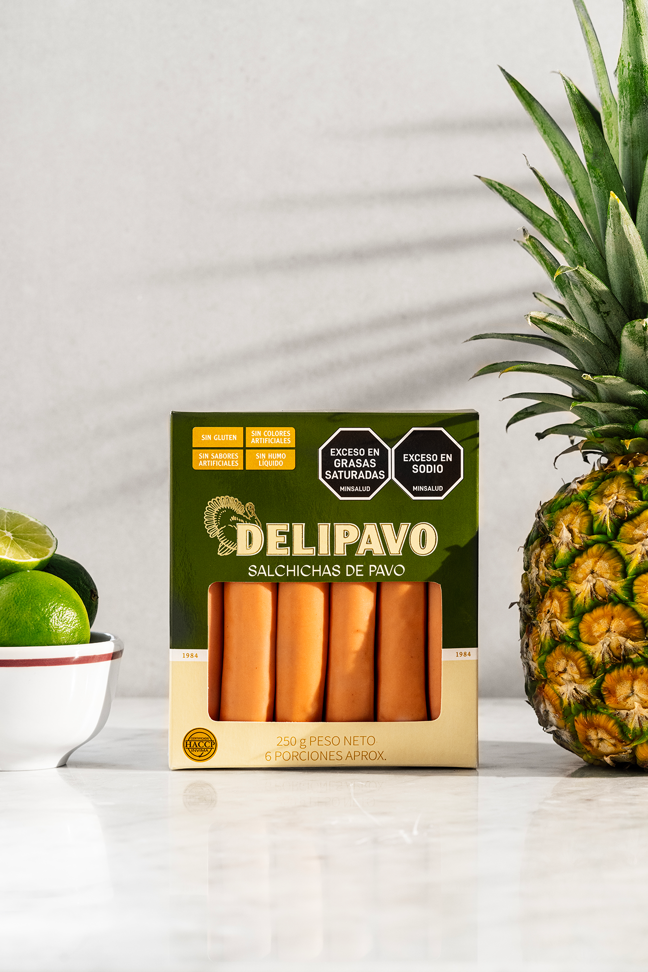 Salchichas de Pavo Delipavo en empaquetado, acompañadas de piña y limón en una mesa, saludable y artesanal.