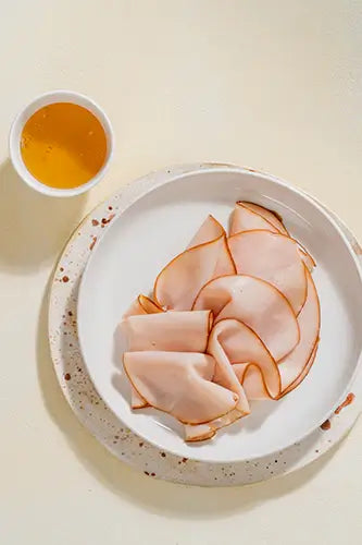 Rebanadas de Pechuga de Pavo Ahumada con Miel servidas en un plato con miel.